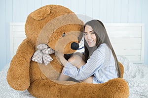 Asian girl sleeping on the bed with a big brown teddy bear.
