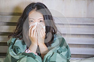 Sweet Asian Korean girl in pajamas covered with blanket sick suffering cold and flu taking temperature with thermometer in bed