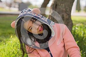 Sweet Asian woman in hoodie making faces - lifestyle portrait of young happy and beautiful Korean girl sitting playful on green