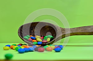 Sweet assorted multicolored chocolates, gum balls in a wooden spoon on a green photon or tablets and vitamins.