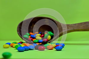 Sweet assorted multicolored chocolates, gum balls in a wooden spoon on a green photon or tablets and vitamins.