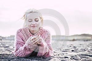 Sweet attractive cheerful and thoughtful blonde yong woman lay down at the beach on the sand to enjoy the freedom and the leisure