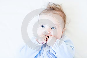 Sweet baby in a blue knitted sweater sucking on its hand