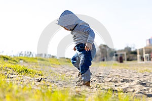 Sweet baby boy in hoodie and jeans walking and playing in the sand. Activity with toddler