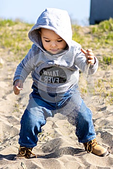 Sweet baby boy in hoodie and jeans walking and playing in the sand. Activity with toddler