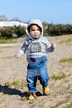 Sweet baby boy in hoodie and jeans walking and playing in the sand. Activity with toddler