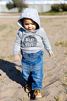 Sweet baby boy in hoodie and jeans walking and playing in the sand. Activity with toddler