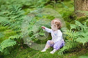 Sweet baby girl gathering wild raspberries in forest