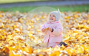 Sweet baby girl playing with leaves and laughing in park