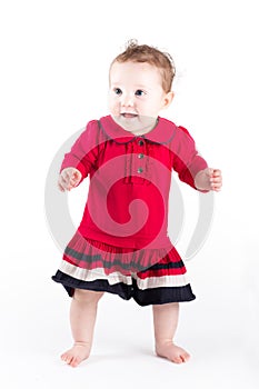 Sweet baby girl in red dress making her first steps