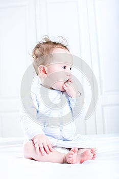 Sweet baby girl sucking on her finger sitting in a white nursery