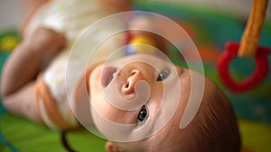 Sweet baby playing toy. Close up of cute baby boy lying on colorful mat. Portrait of adorable baby. Happy infant study