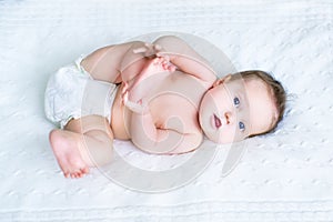 Sweet baby wearing a diaper playing with her feet