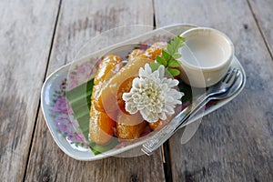 Sweet bananas serve with coconut syrup on the plate and wooden table.