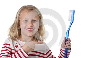 Sweet beautiful female child with blond hair and big blue eyes holding huge toothbrush smiling happy