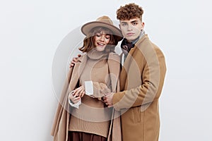 a sweet, beautiful, loving couple stands on a white background in stylish beige autumn clothes, gently cuddling up to