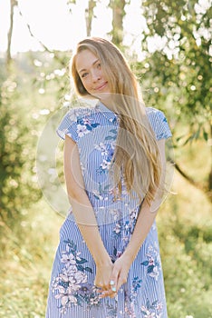 A sweet and beautiful young smiling woman in a blue dress with flowers and long blonde hair. Summer portrait of a happy girl