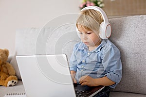 Sweet blond child, boy in casual clothes, woring on computed at home