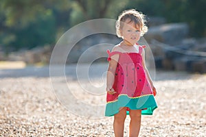 Sweet blond little baby girl in beautiful dress plays walks outdoors