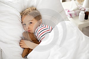 Sweet blond preschool child with teddy bear, lying in bed sick
