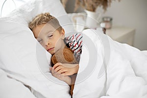 Sweet blond preschool child with teddy bear, lying in bed sick