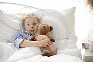 Sweet blond preschool child with teddy bear, lying in bed sick