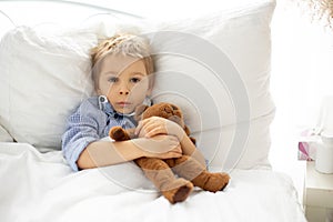 Sweet blond preschool child with teddy bear, lying in bed sick