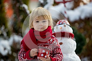 Sweet blond toddler child, boy, playing in garden with snow, making snowman, happy kid winter time