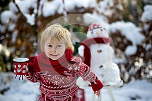Sweet blond toddler child, boy, playing in garden with snow, making snowman, happy kid winter time