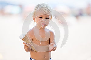 Sweet blonde toddler boy, eaiting ice cream on the beach