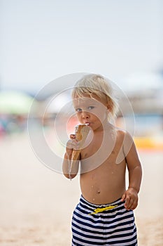 Sweet blonde toddler boy, eaiting ice cream on the beach