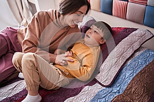 Sweet boy with Down syndrome laying at the bed while playing with his mother