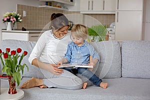 Sweet boy and his mom, reading a book at home, sitting on the couch, relaxing, mom working from home