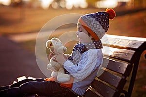 Sweet boy, sitting on bench with teddy bear on sunset