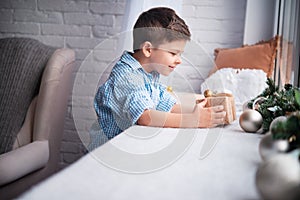 The sweet boy at the window is looking at the gift box. The atmosphere of the New Year or Christmas