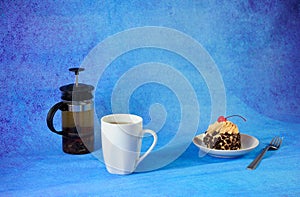 Sweet breakfast, tea cup plate with sponge cake in chocolate chips with cherries and tea teapot on a blue abstract background