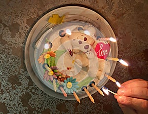 Sweet cake with candles. A hand holds a match with fire for lighting candles on cake.