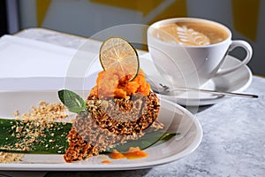 Sweet cake decorated with dry lemon. Cup of coffee. Delicious condensed milk cake with mango on plate on table