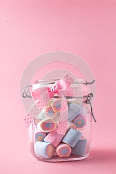 Sweet candy marshmallows in bank on jar on pink pastel background.