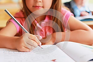 A sweet Caucasian child in school at a desk writes in a notebook