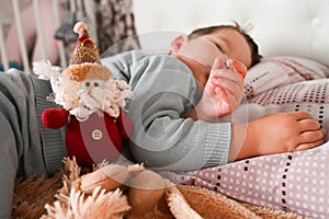 Sweet caucasian toodler boy sleeping in his bed next to a toy gnome. Christmas morning concept