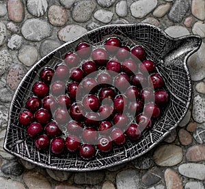 Sweet cherry, cherry, sweet cherry in beautiful plates in the form of a leaf on a stone background,