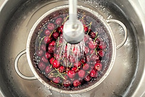 Sweet cherry washing in metal colander in the kitchen sink.
