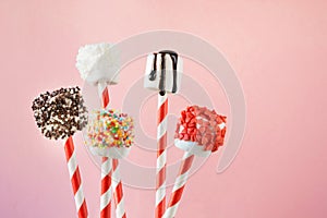 Sweet chewy marshmallow and lollipops on straw decorated with melted chocolate and cake sprinkles on pink background. Kids will lo