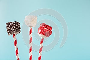 Sweet chewy marshmallow on straw decorated with melted chocolate and cake sprinkles on blue. Copy space. Holiday card.