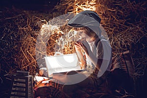 Sweet child, boy, reading a book on the attic on a house, sitting on a hay of straw