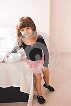Sweet child girl 2-3 year old wearing ballet shoes and bodysuit in room. Practice dancing at home. Childhood. Preschool