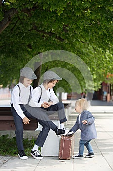 Sweet children in vintage clothing, hat, suspenders and white shirts, holding suitcase, running in the park