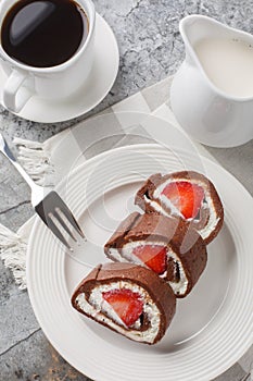 Sweet chocolate cake roll filled with strawberries and cream cheese served with coffee close-up. Vertical top view
