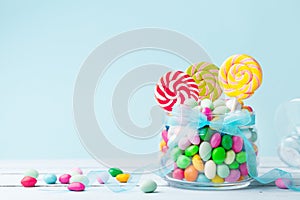 Sweet colorful candy in jar decorated with bow ribbon against blue background. Gifts for Birthday party.